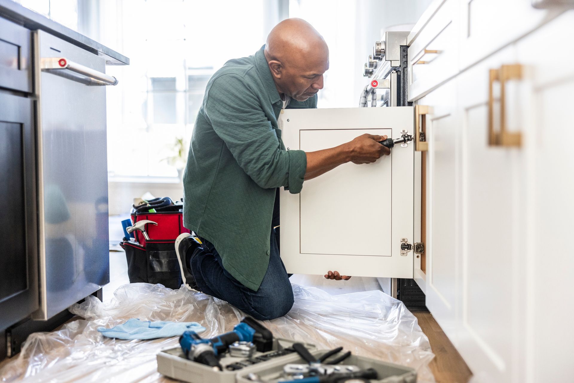 Senior man repairing kitchen cabinet at home.