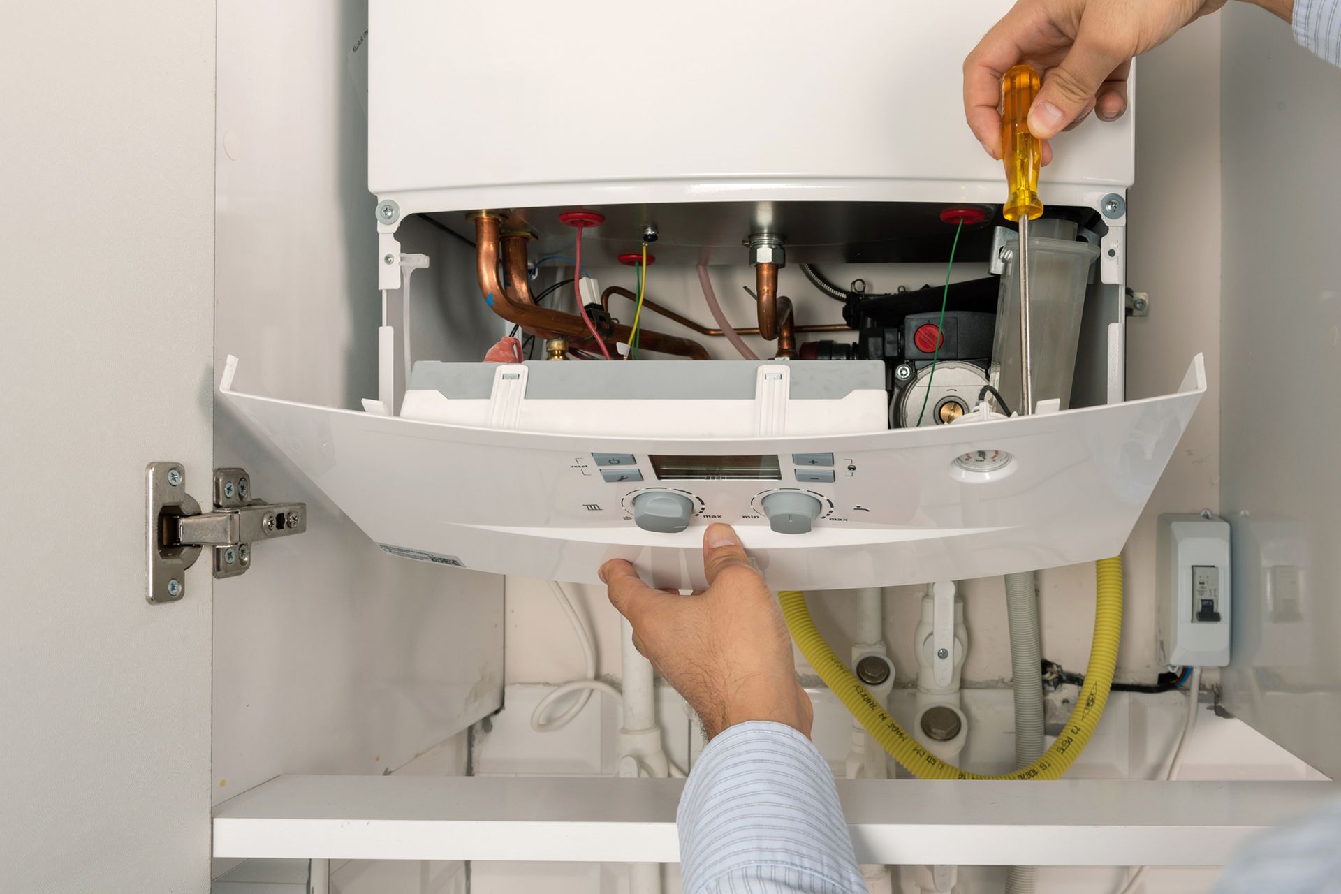 A person is fixing a boiler with a screwdriver.