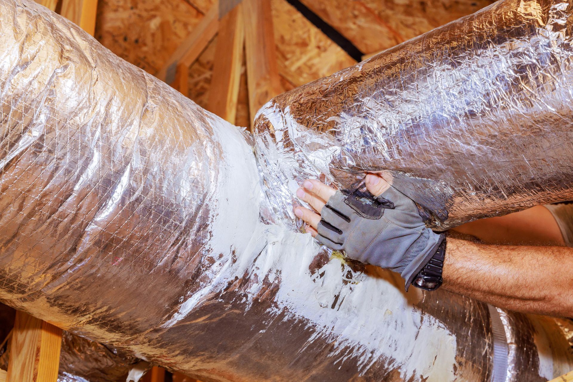 A man is wrapping a duct with aluminum foil.