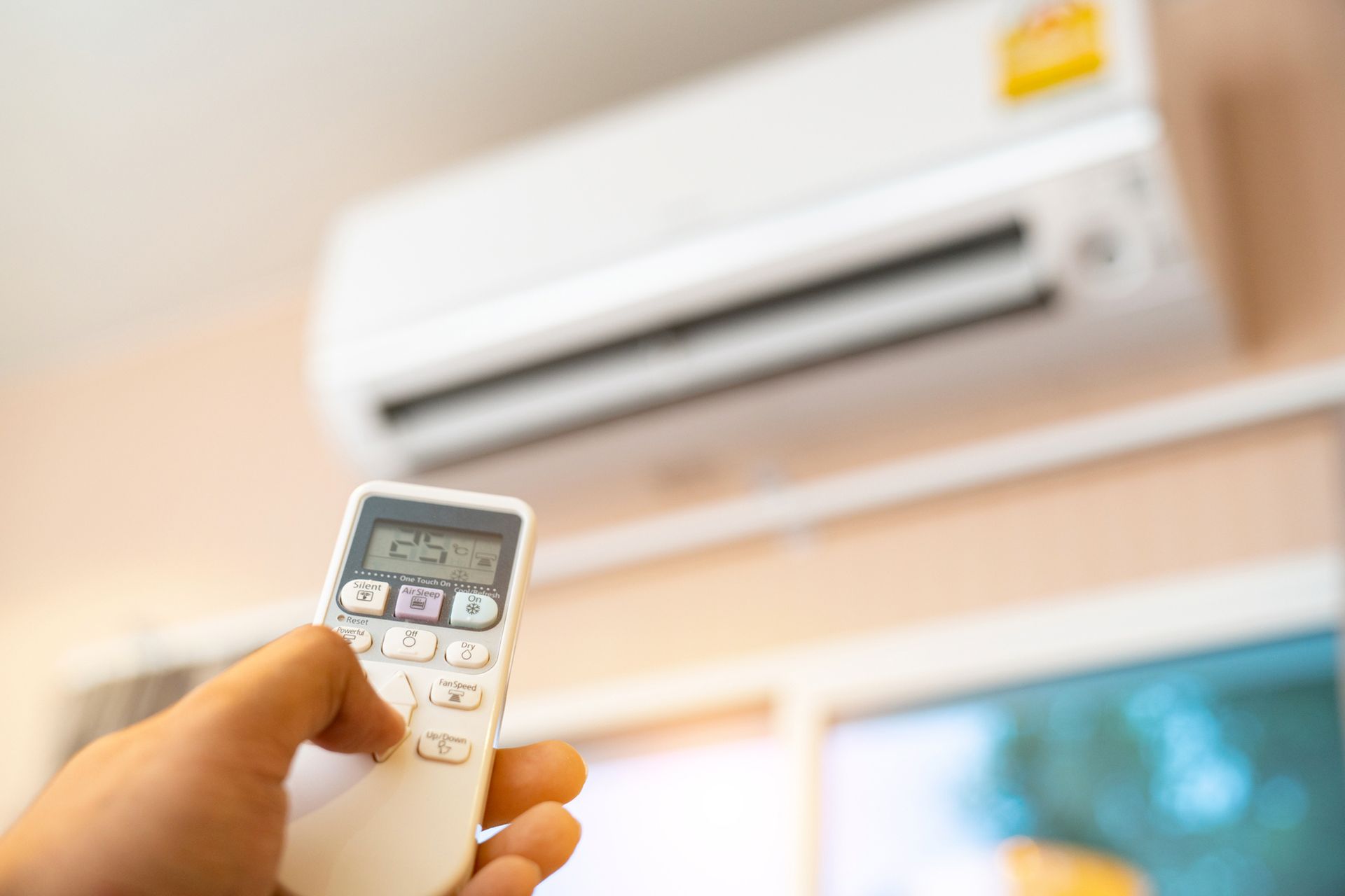 A person is holding a remote control in front of an air conditioner. A person is holding a remote control in front of an air conditioner.