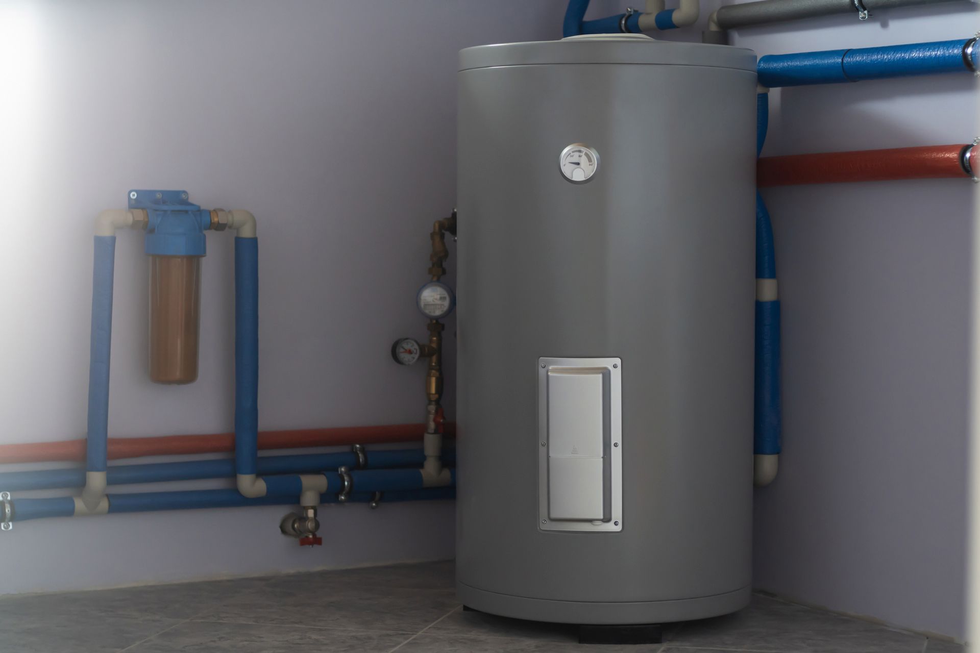 A water heater is sitting in a room next to pipes.