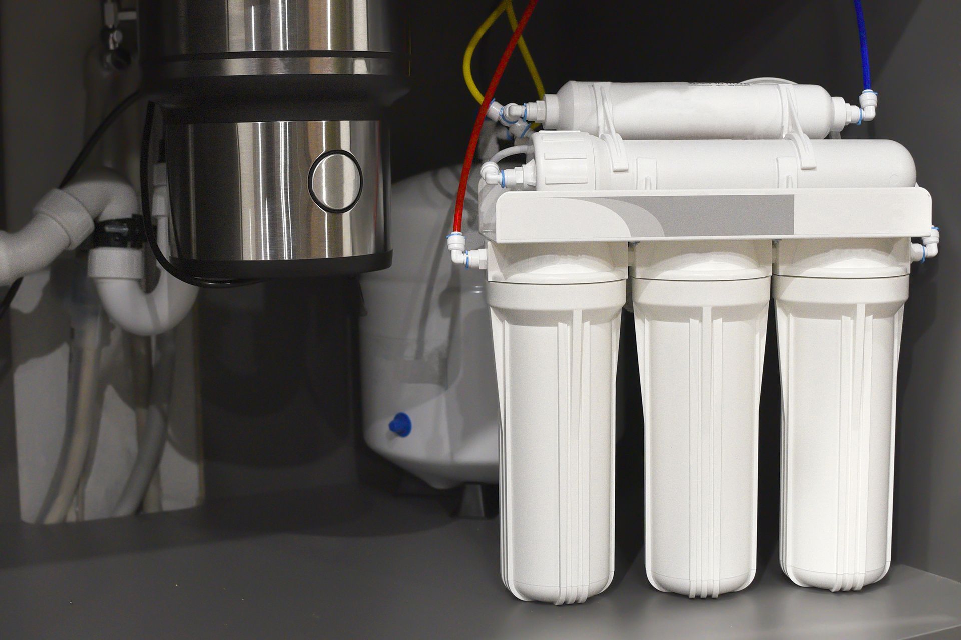 A water filter is sitting under a sink in a kitchen. A water filter is sitting under a sink in a kitchen.