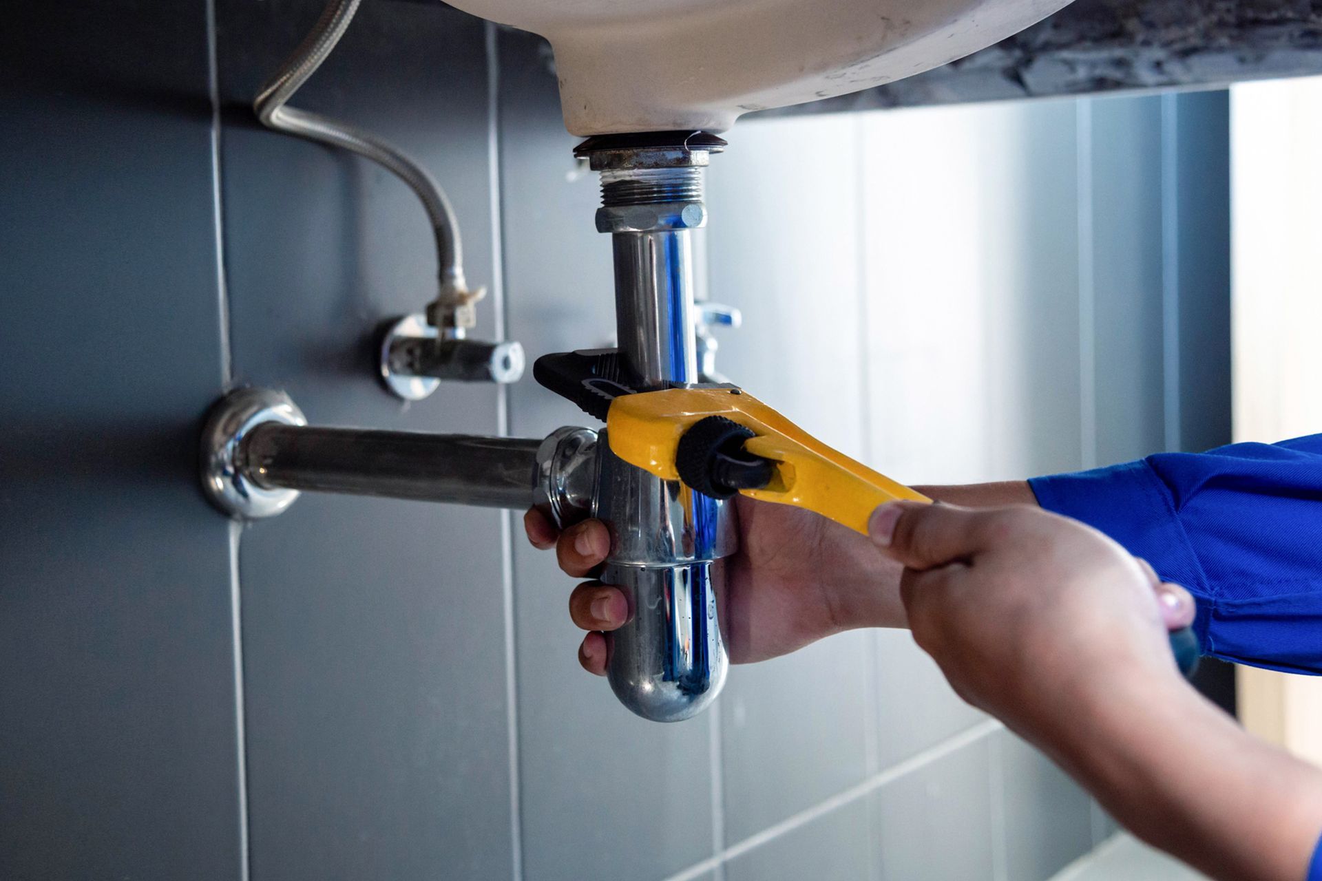 A plumber is fixing a sink pipe with a wrench. A plumber is fixing a sink pipe with a wrench.