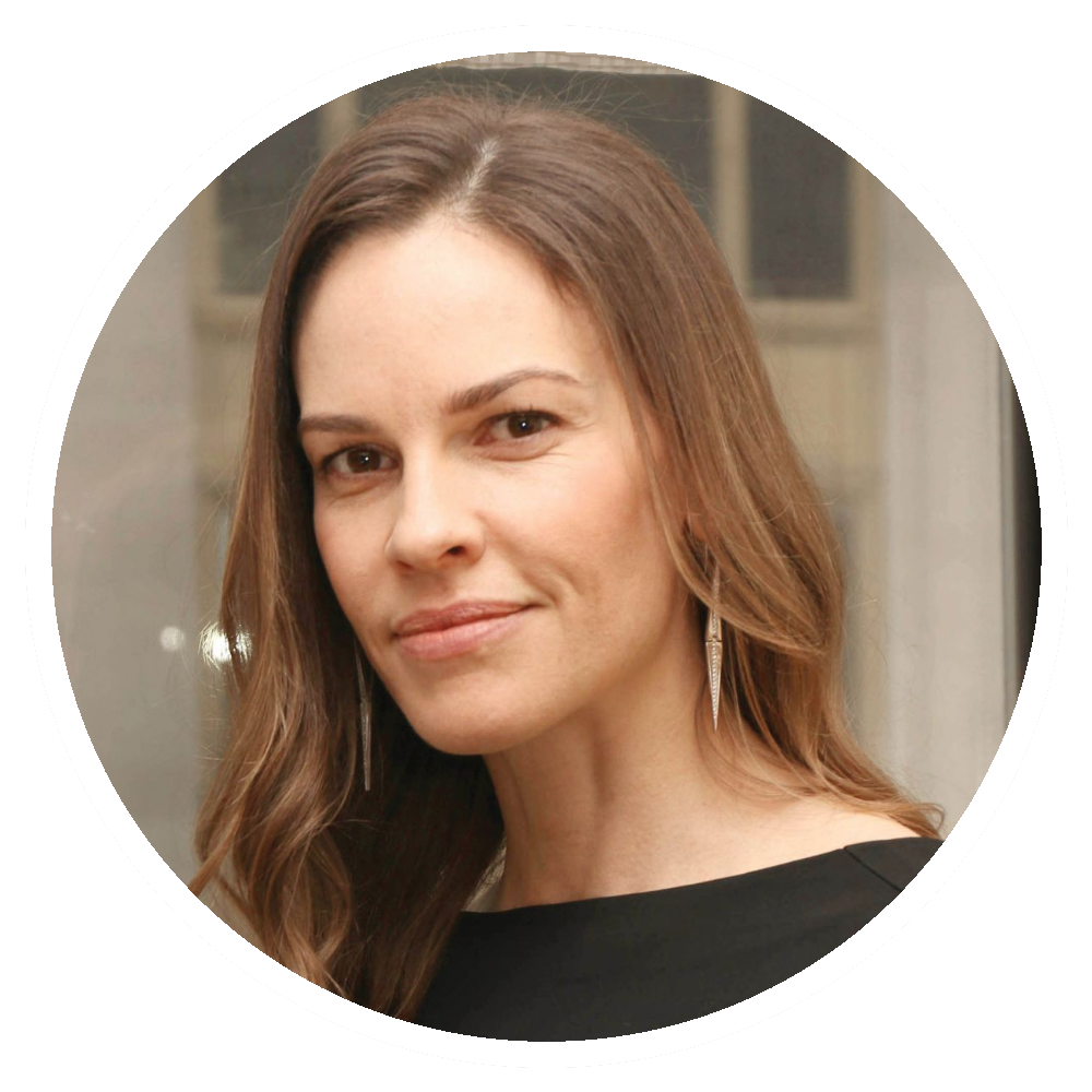 Hilary Swank with long brown hair, wearing a black top, smiling.