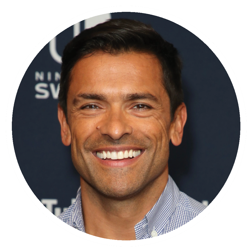 Mark Consuelos with short dark hair smiles, wearing a light blue button-down shirt.