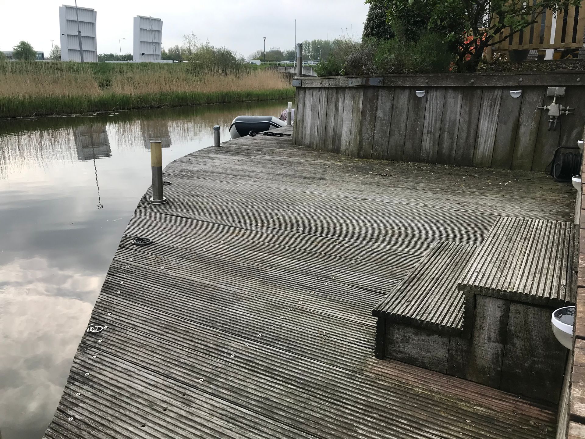 Een houten terras met een gebogen rand, met uitzicht op een rustige rivier, voorzien van vloerplanken met een bijzondere structuur en een trap.