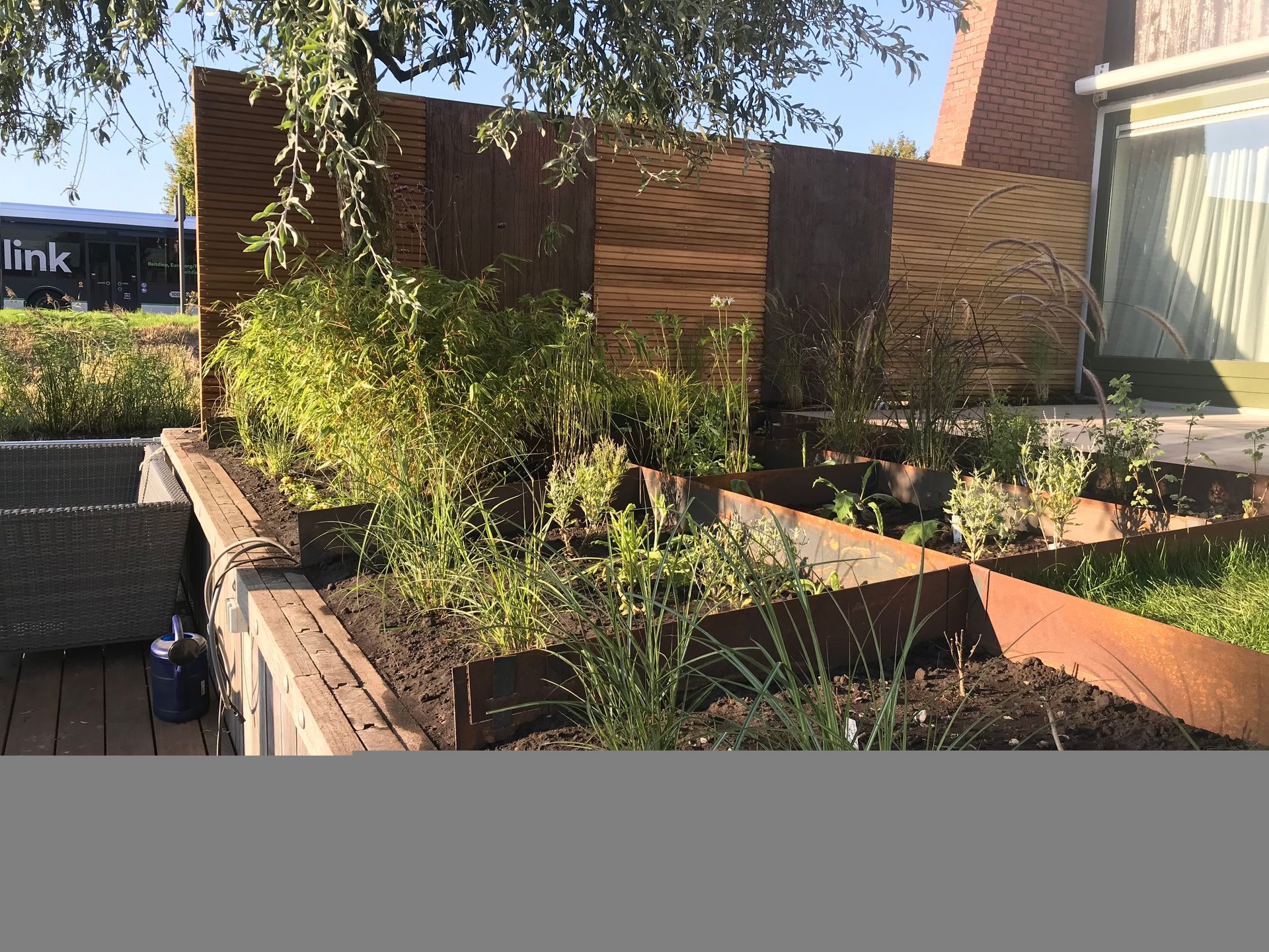 Verhoogde plantenbedden met weelderig groen voor een moderne, veelzijdige houten schutting op een zonnige dag.