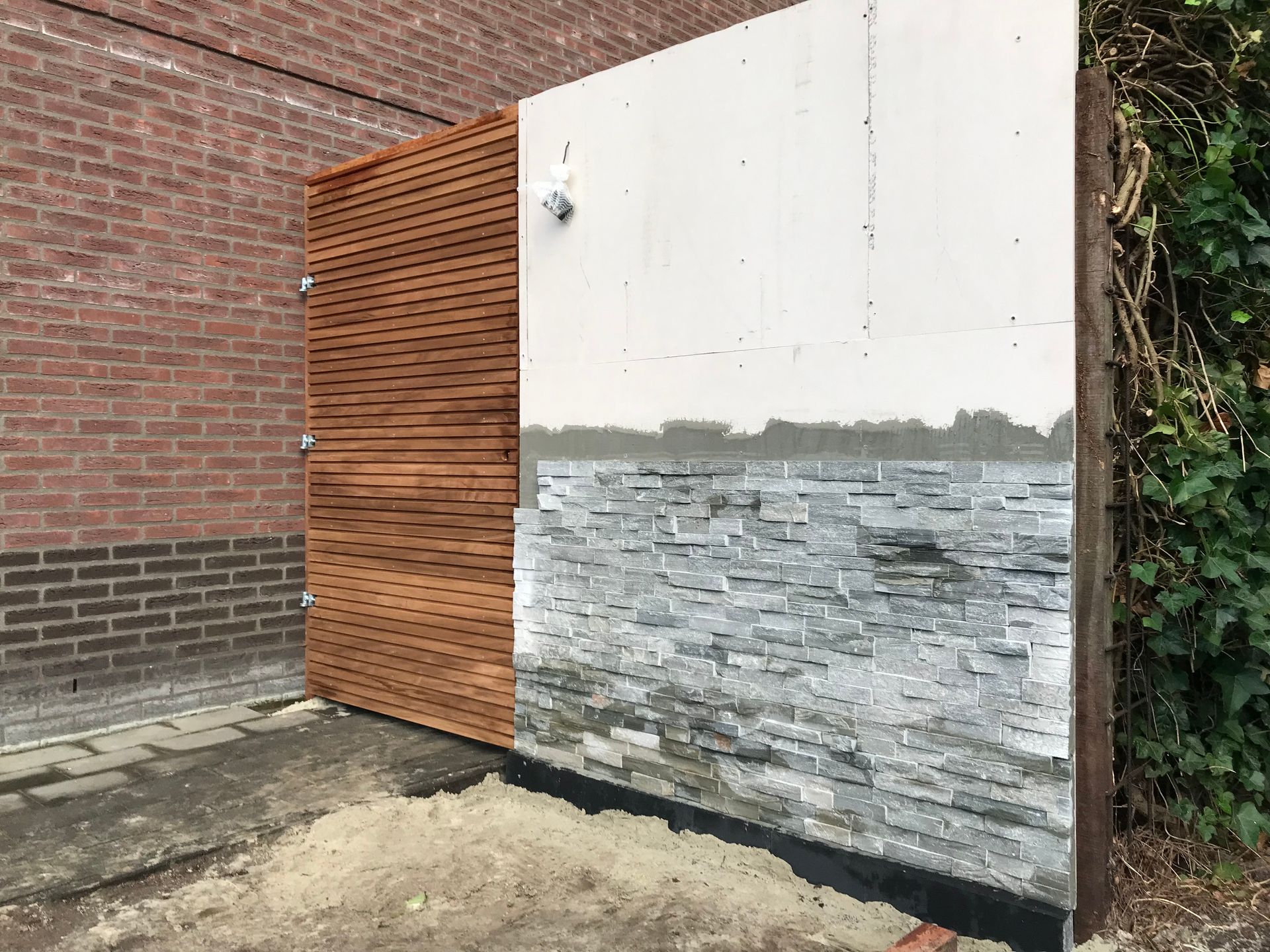 Een wandgedeelte met houten latten aan de linkerkant en een halfafgewerkte stenen bekleding over een wit paneel aan de rechterkant.