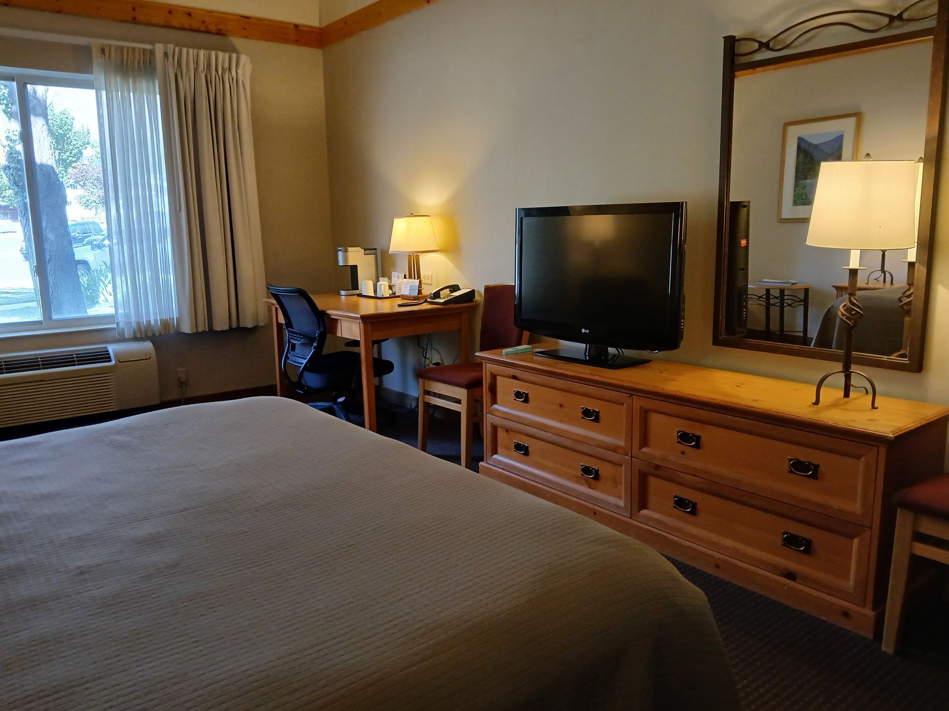 A hotel room with a bed , desk , television and mirror