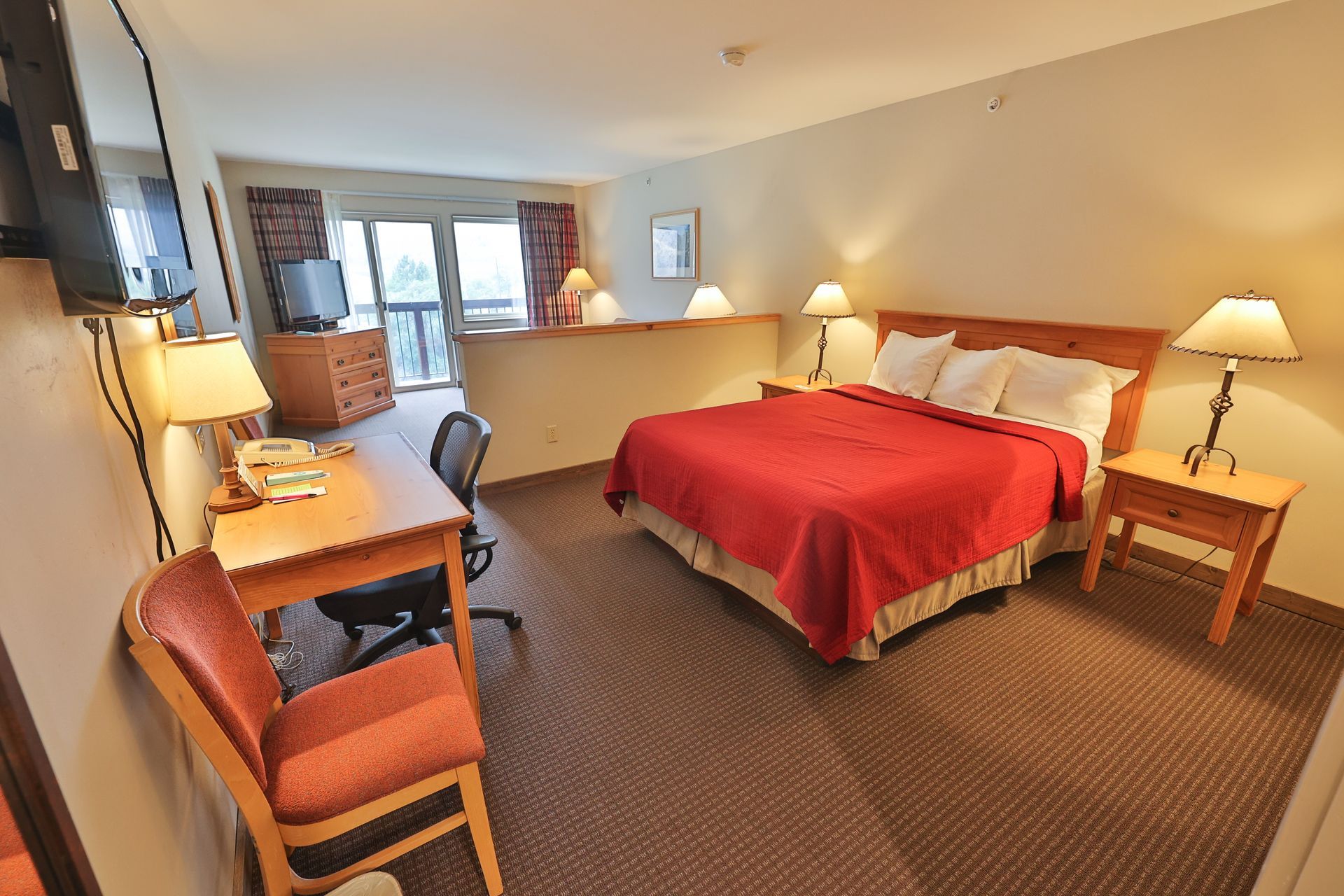 A hotel room with a king size bed , desk , chair and television.