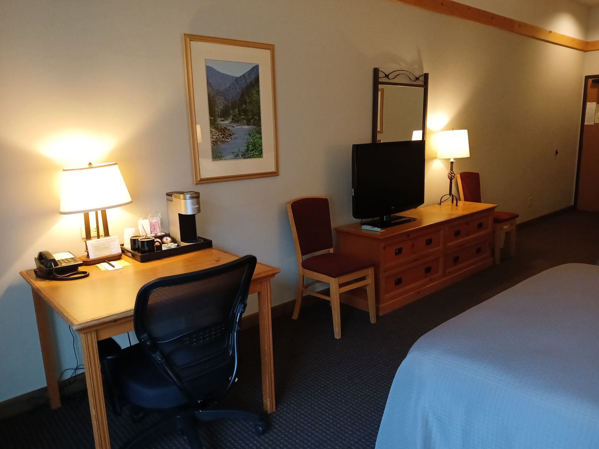 A hotel room with a desk a chair and a television