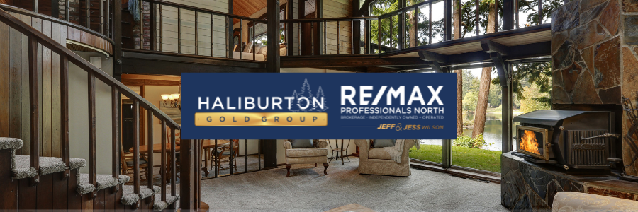 Interior view of a house with a fireplace, staircase, and large windows.  The RE/MAX Haliburton Gold Group logo is in the foreground.