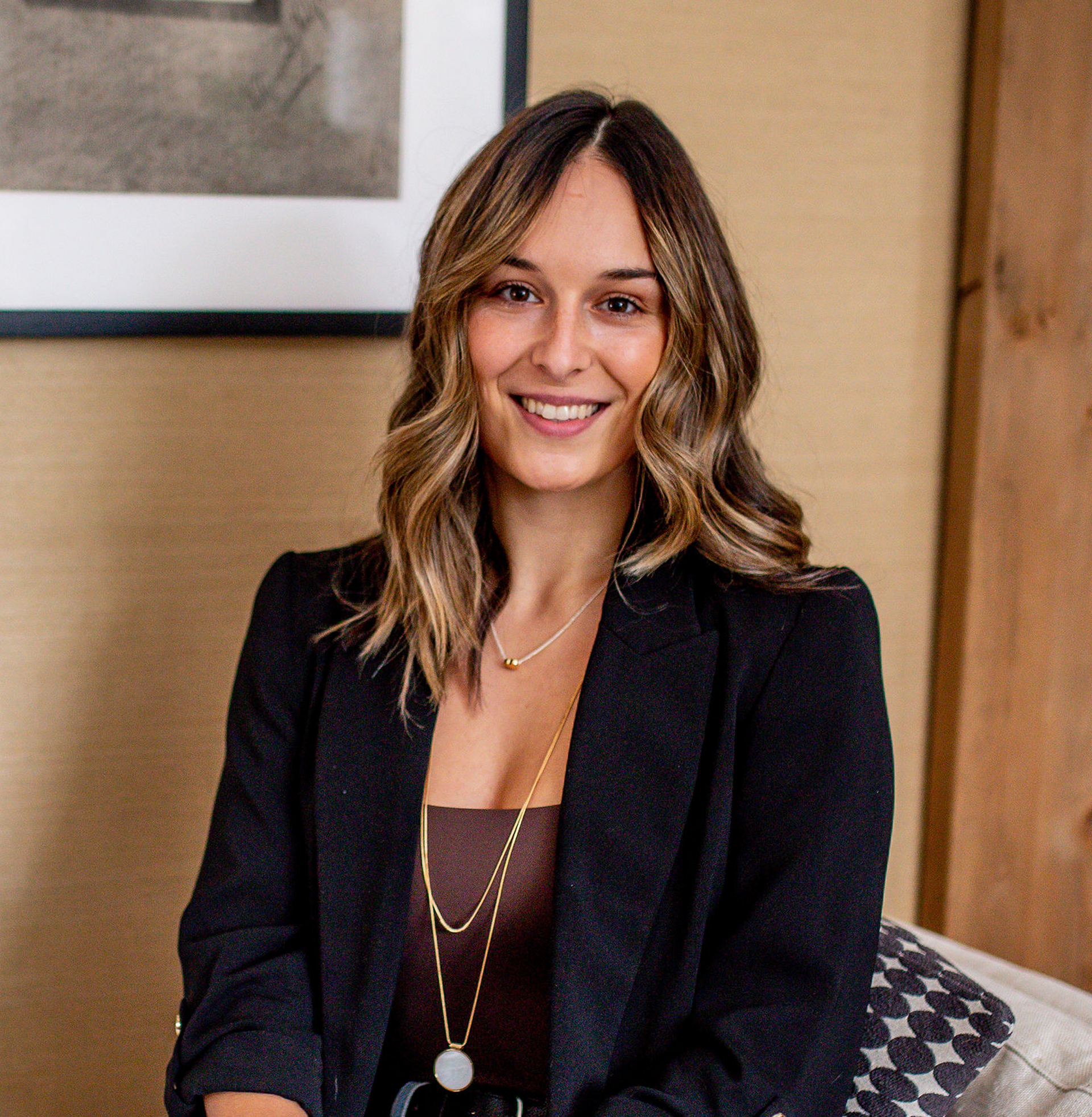A woman is sitting in a chair wearing a black jacket and a necklace.