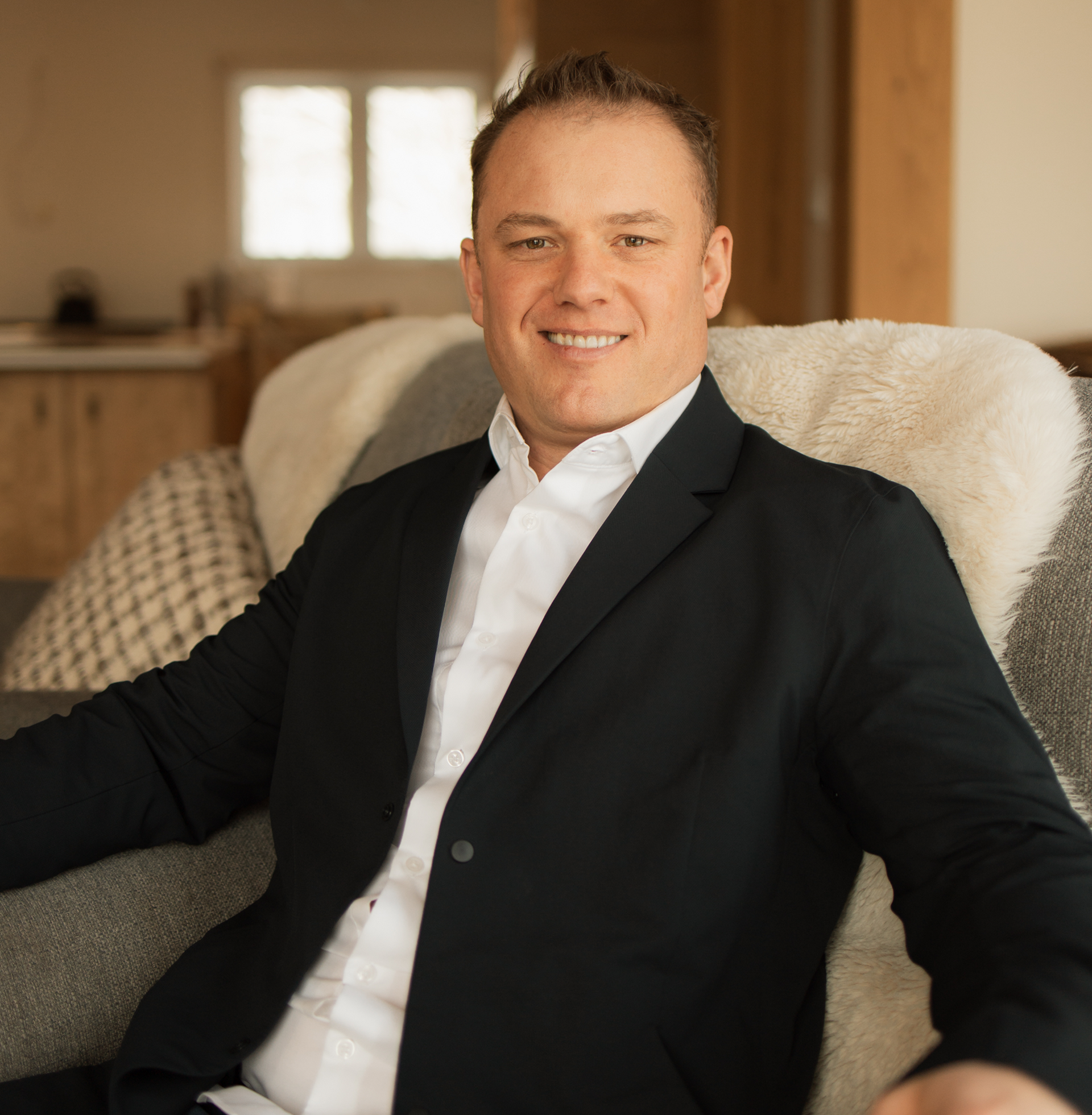 A man in a suit is sitting in a chair and smiling