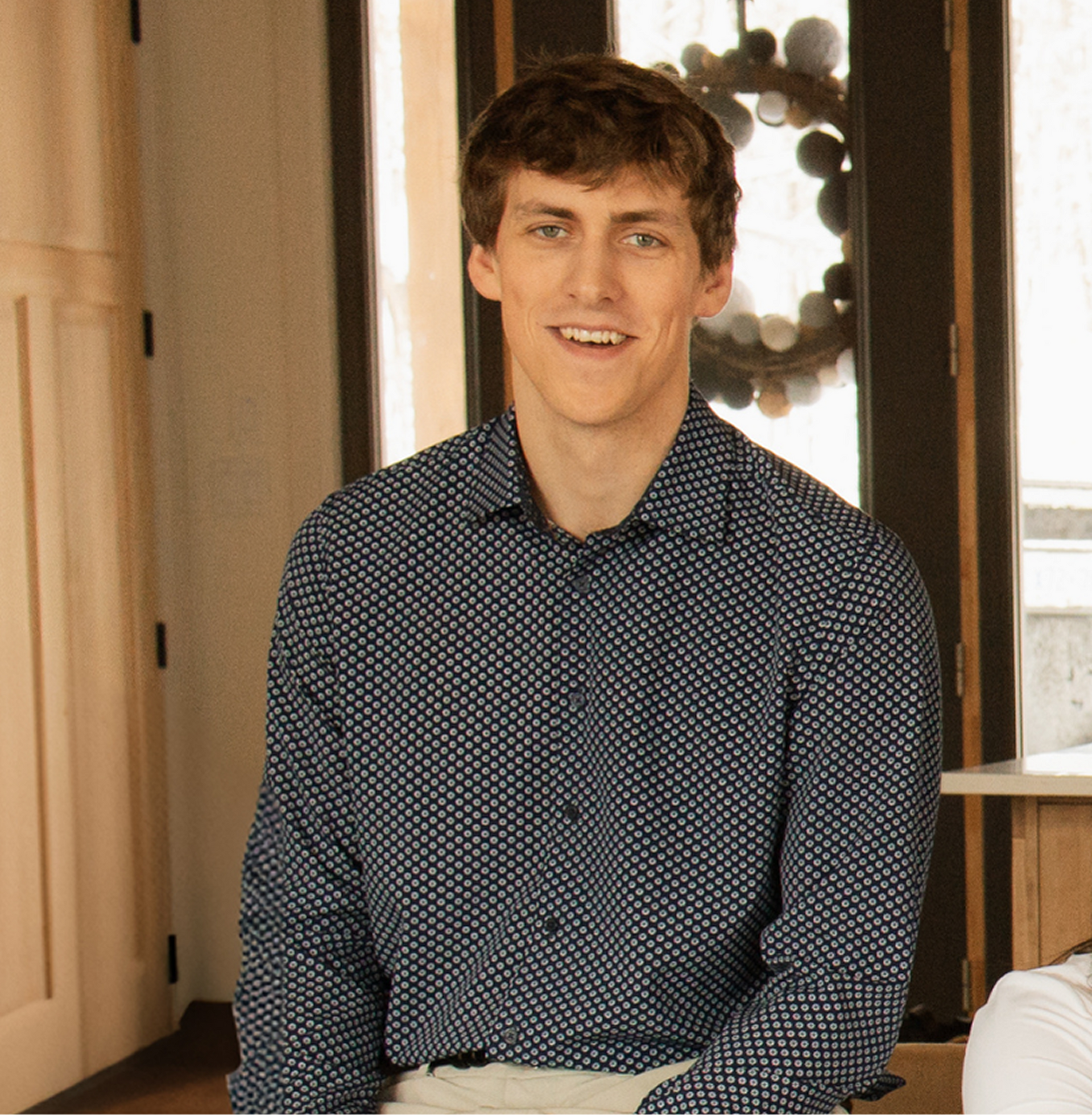 A man in a blue shirt is sitting in front of a window