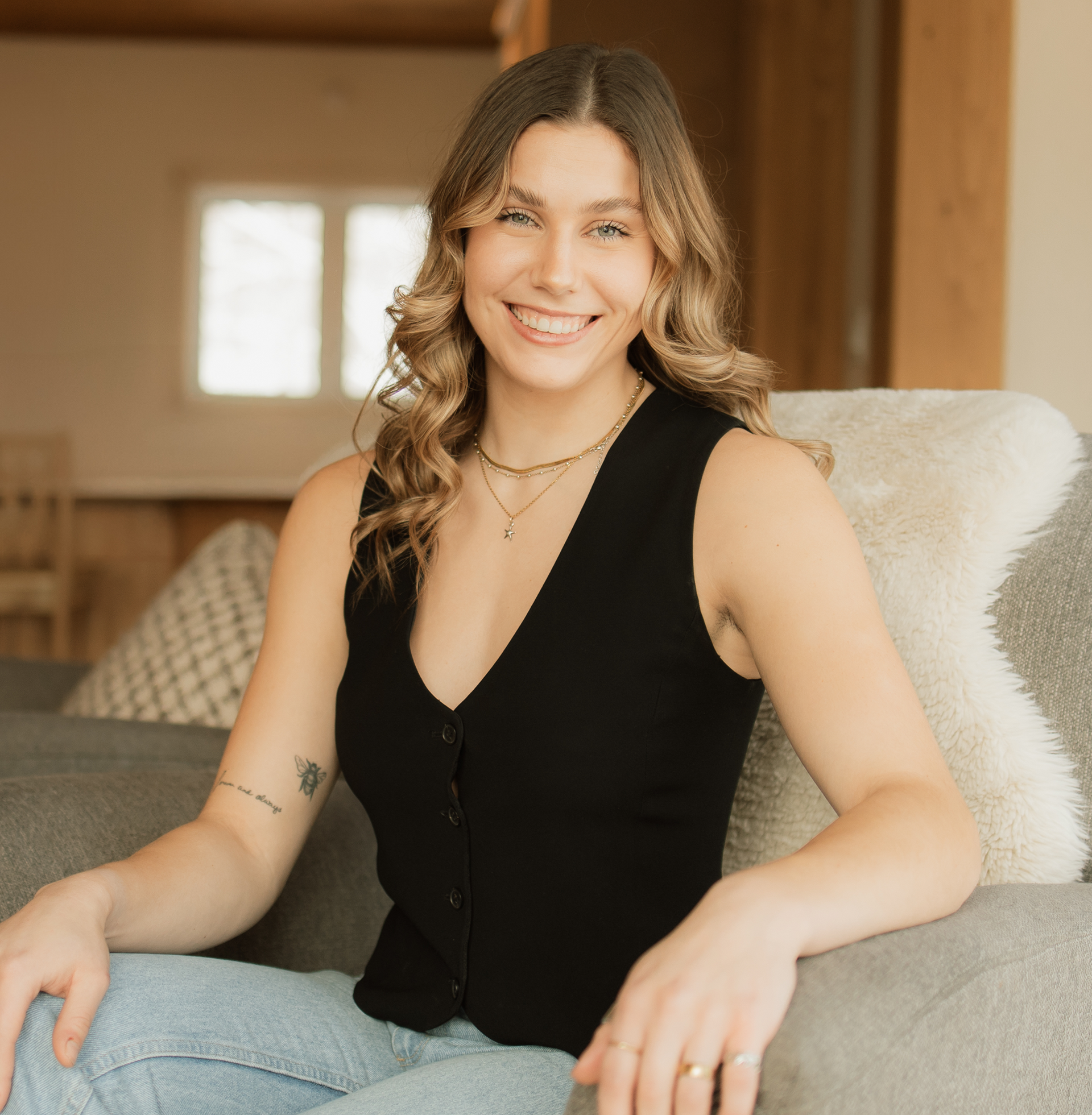 A woman in a black tank top is smiling while sitting on a couch