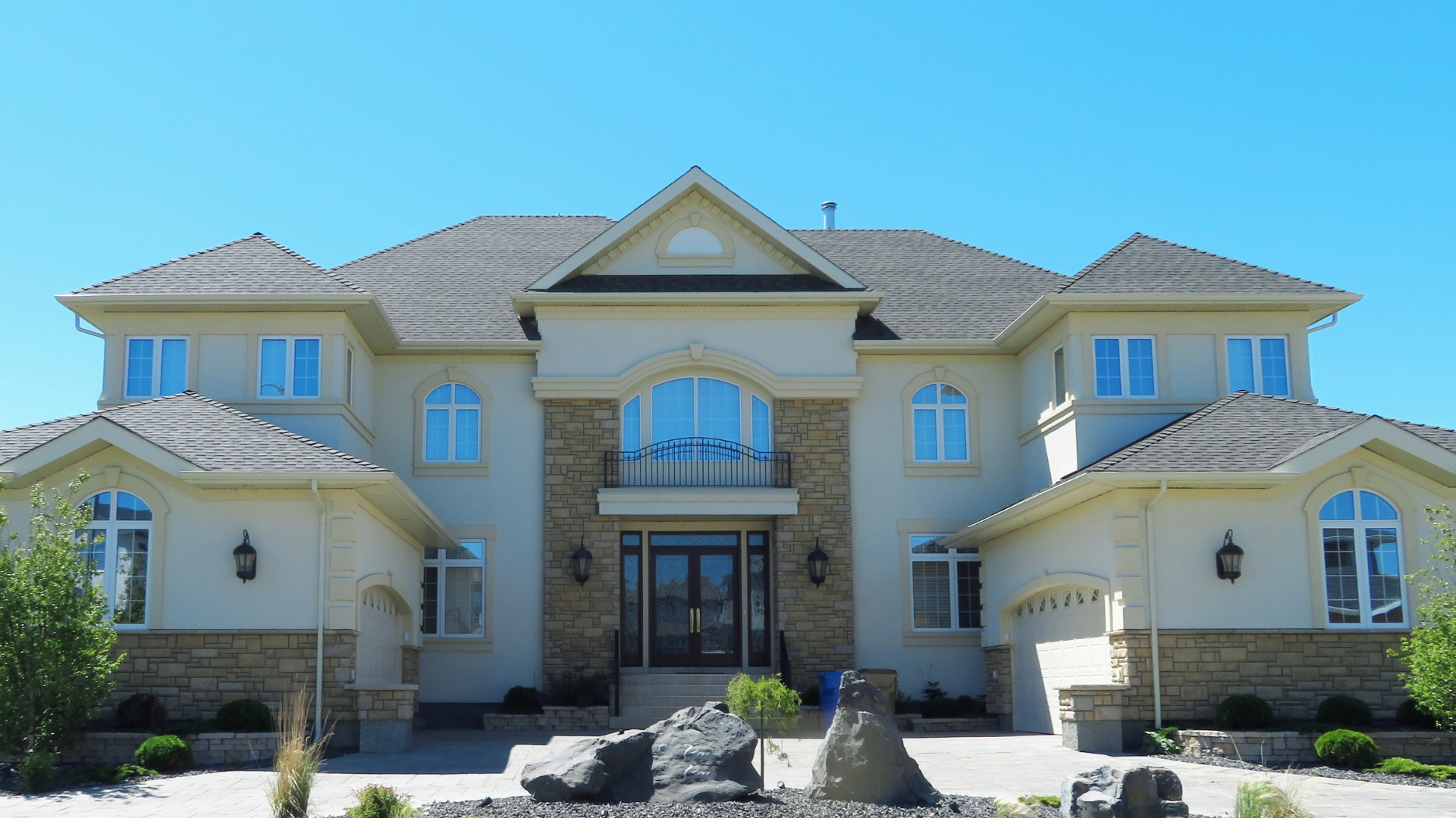 Large beige stone mansion with a symmetrical facade, arched windows, and a central double-door entrance