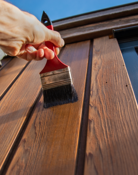 A person is painting a wooden wall with a brush.