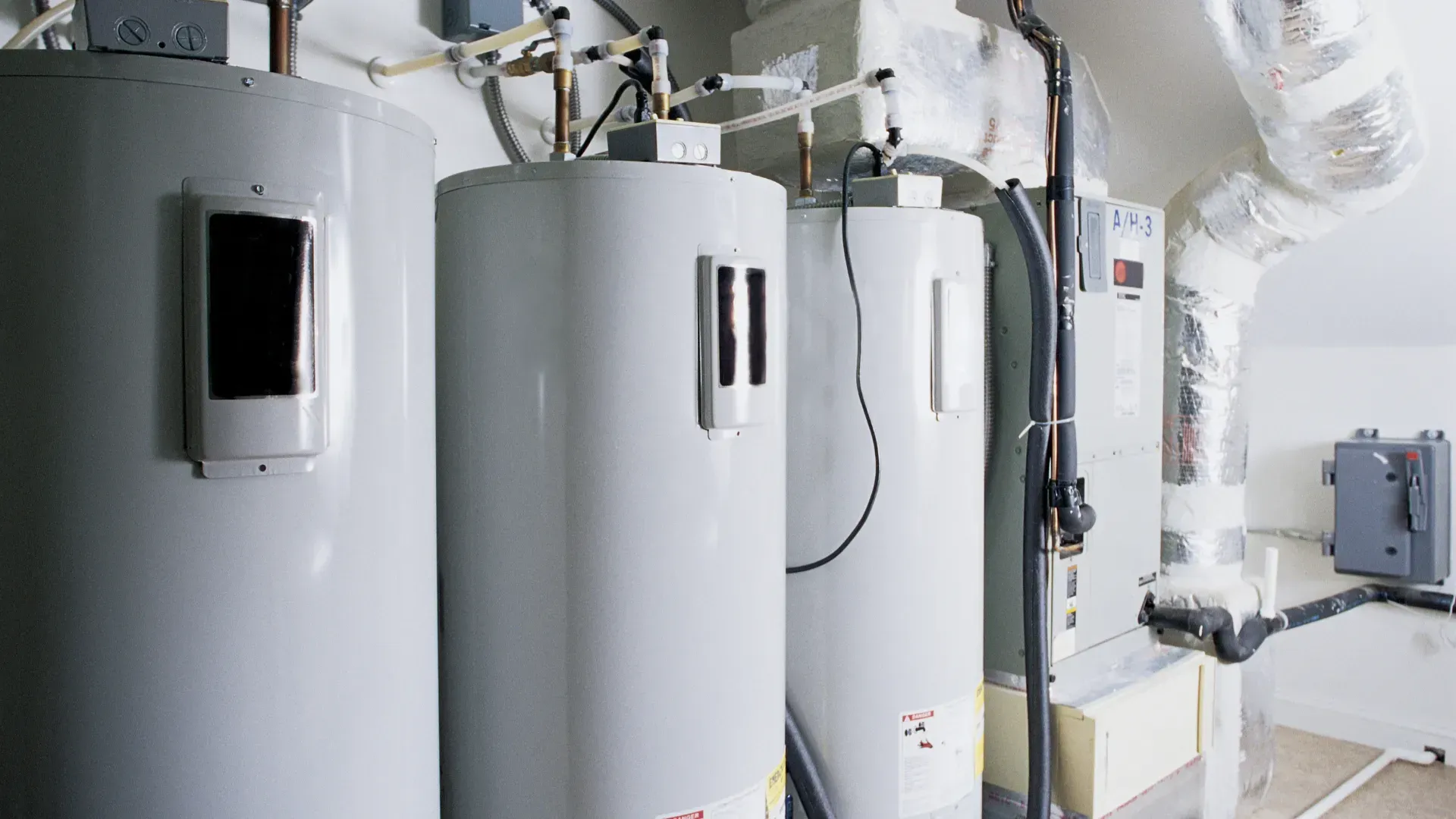 Three water heaters are sitting next to each other in a room.