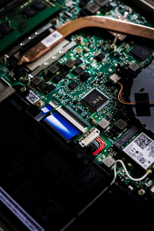 Close-up of a laptop motherboard with visible circuit board, ribbon cable, and components under repair