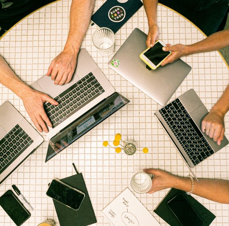 Team collaborating around laptops and coffee on a tiled table, with one person holding a smartphone.