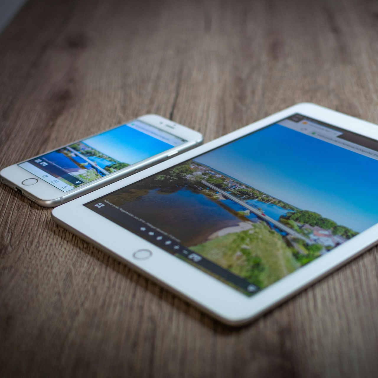 White smartphone and tablet on a wooden table, both displaying the same landscape photo.
