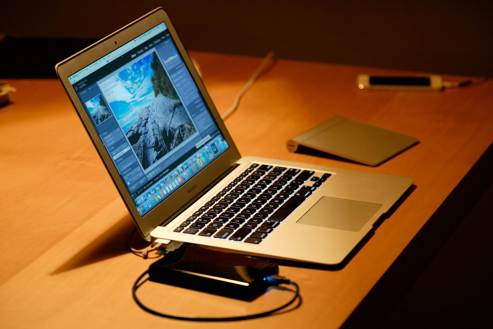 Open laptop on a wooden desk with a cable and small device beside it.