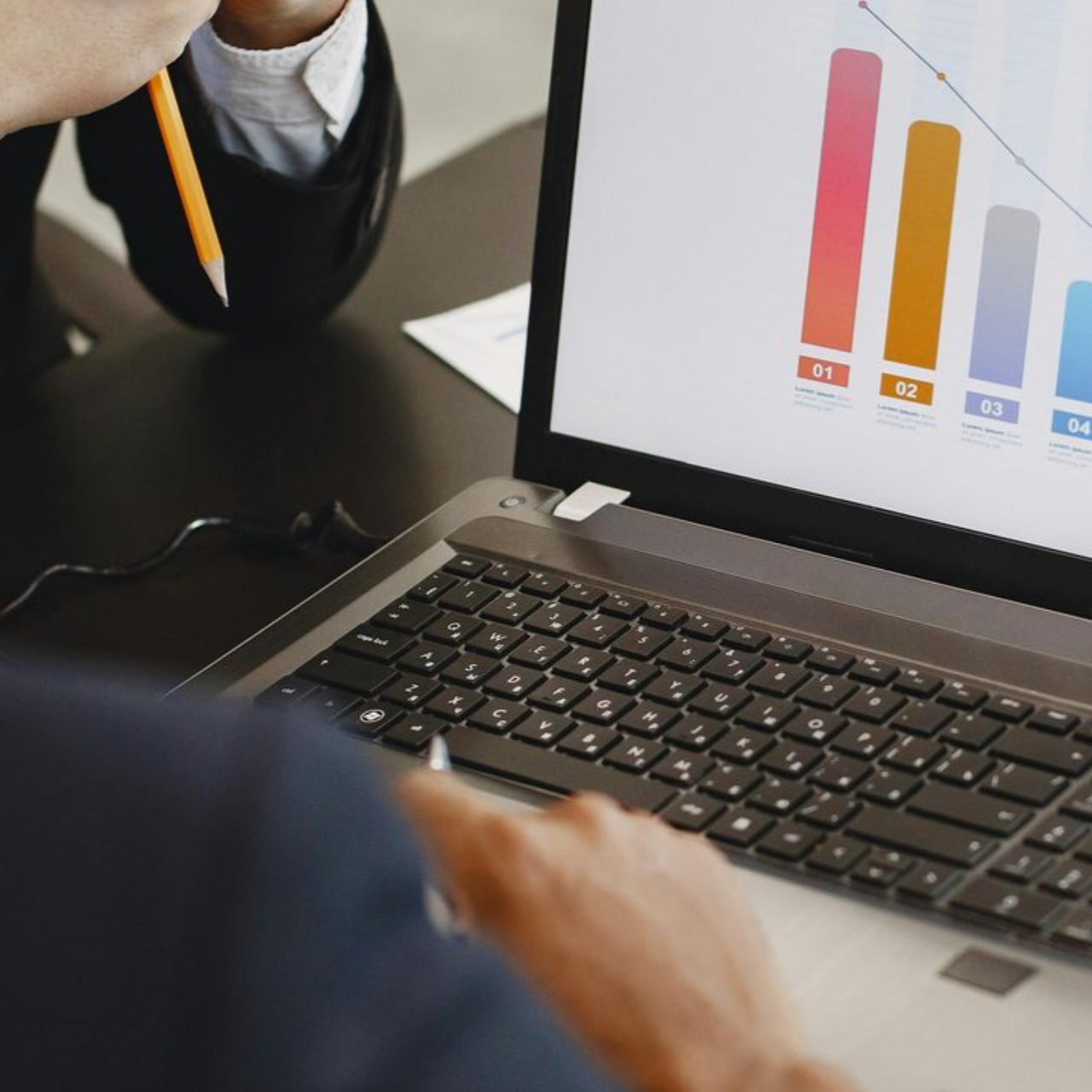 Person pointing at a laptop showing a colorful bar chart in a meeting setting