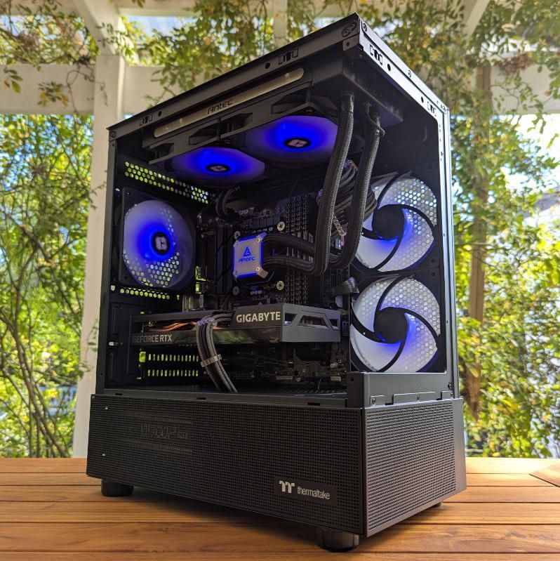 Open desktop PC with blue-lit fans and visible internal components on a wooden table outdoors