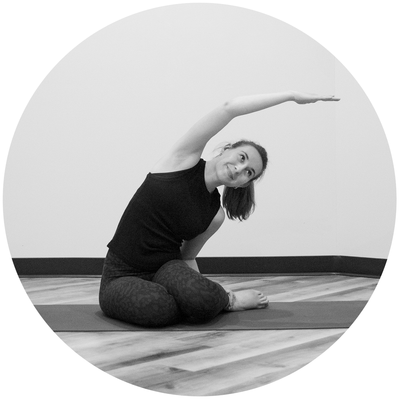 Une femme est assise sur un tapis de yoga, le bras tendu.