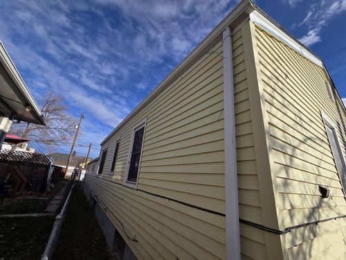 Side view of a beige house with vinyl siding under a blue sky with clouds