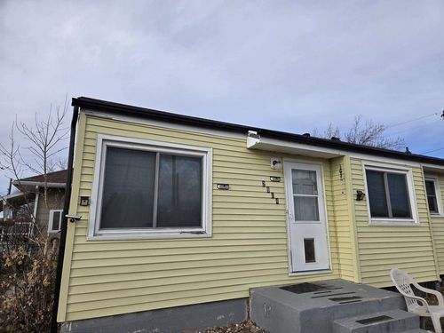 Small yellow house exterior with white door, large windows, and cloudy sky.