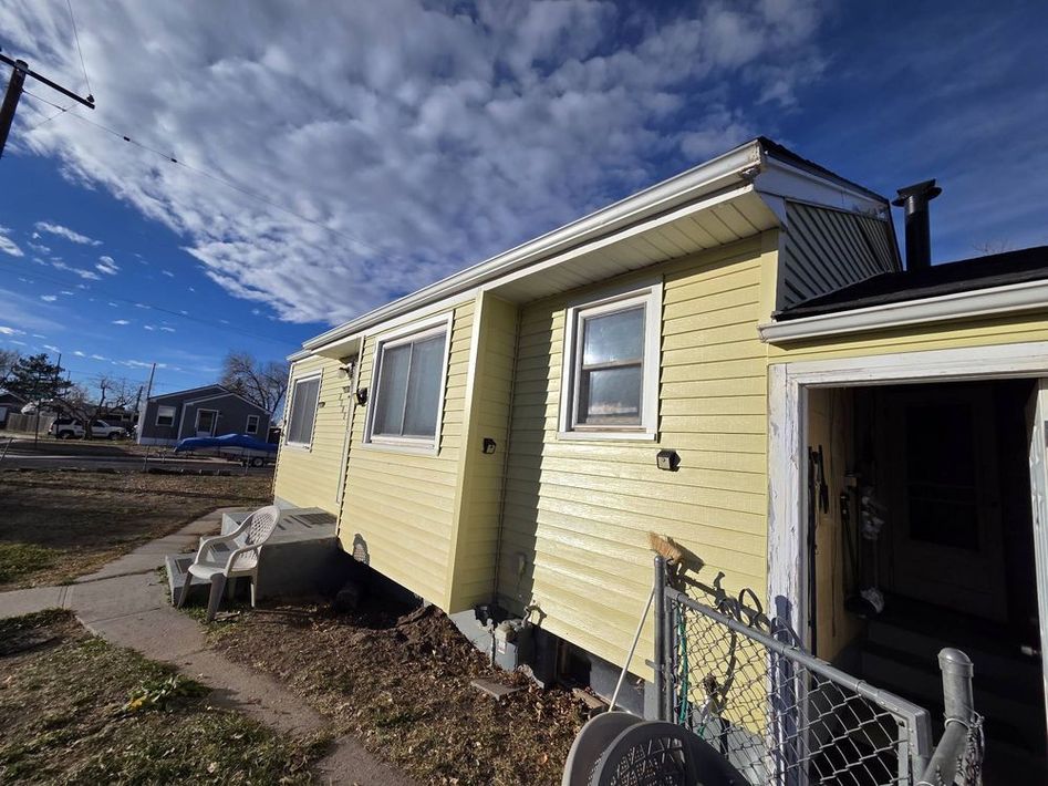 Yellow house exterior with white trim, open doorway, and a cloudy blue sky