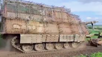 A large tank is driving down a dirt road.