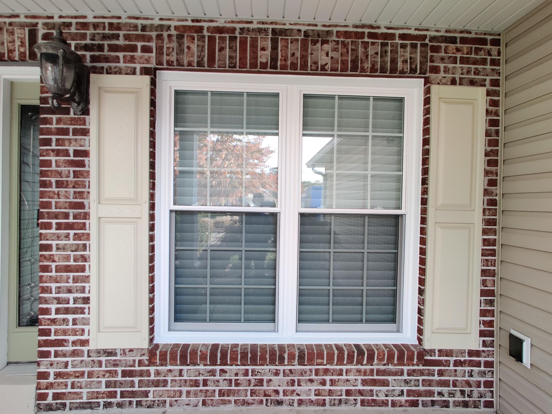 Twin double-hung windows with grids and new white paneled shutters.