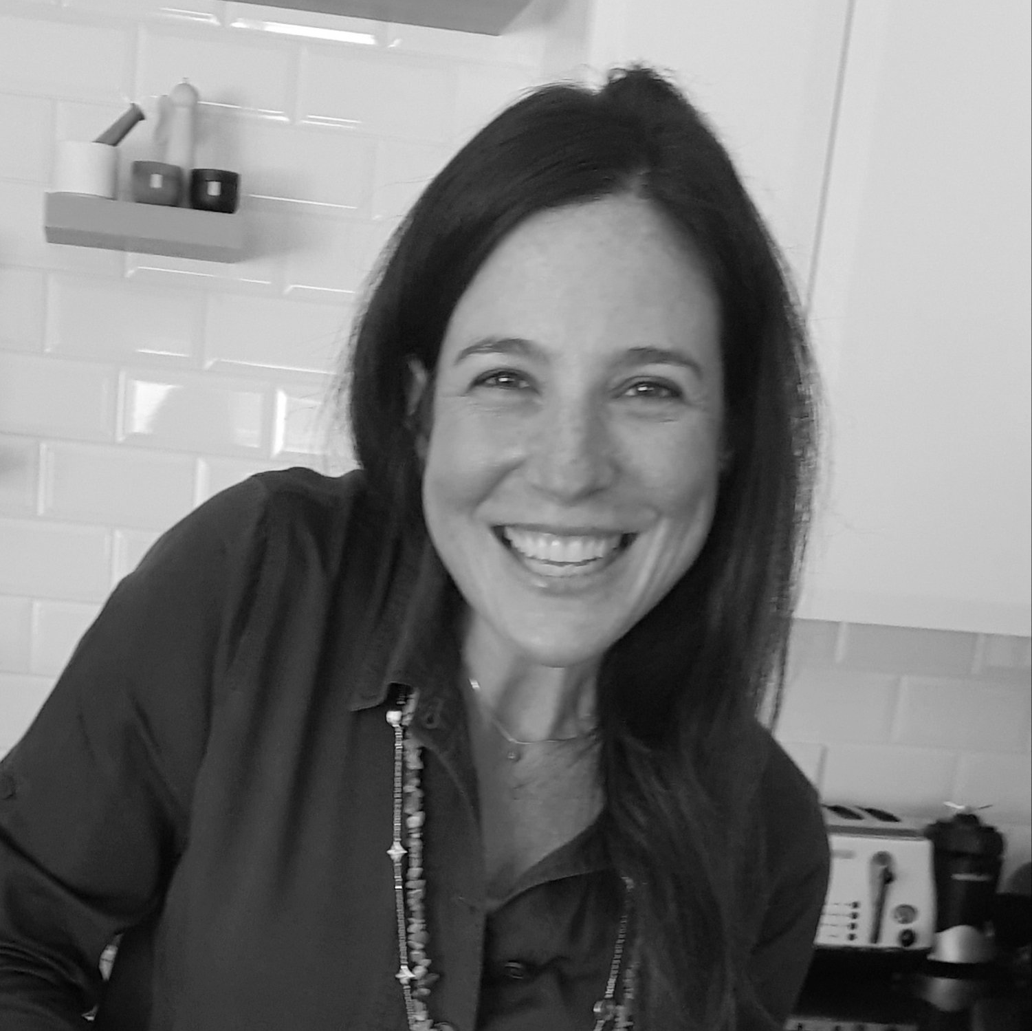 A black and white photo of a woman smiling in a kitchen