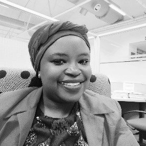 A woman wearing a turban and a jacket is smiling in a black and white photo.