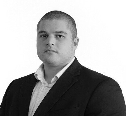 A man in a suit and white shirt is standing in front of a white background.