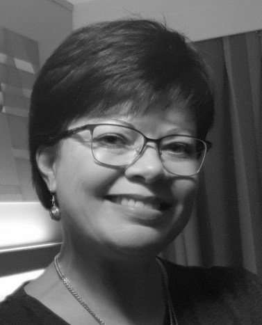 A woman wearing glasses and earrings is smiling in a black and white photo.