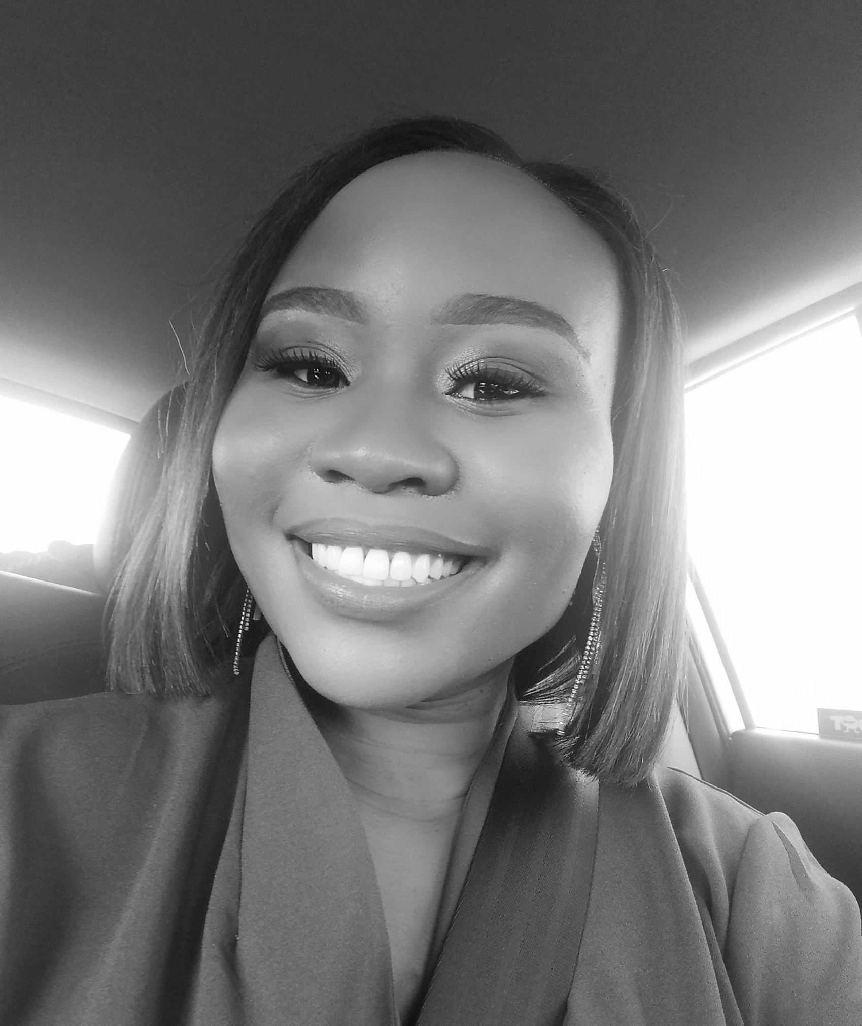 A black and white photo of a woman smiling in a car.