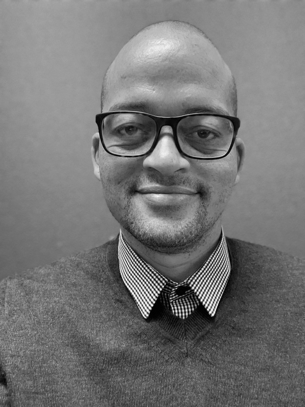 A black and white photo of a man wearing glasses and a sweater.