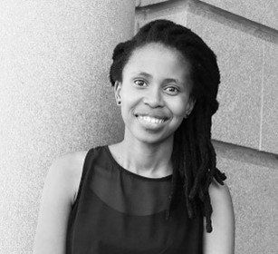 A woman with dreadlocks is smiling in a black and white photo.