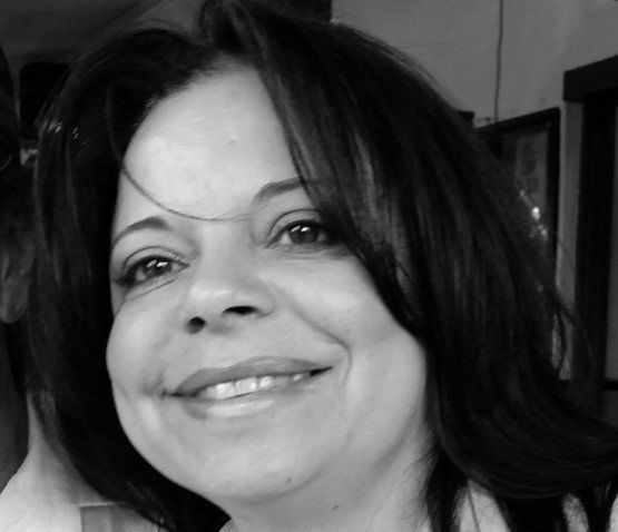 A woman with long dark hair is smiling in a black and white photo.