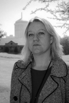 A woman in a coat is standing in front of a building in a black and white photo.