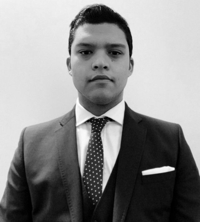 A man in a suit and tie is standing in front of a white wall.
