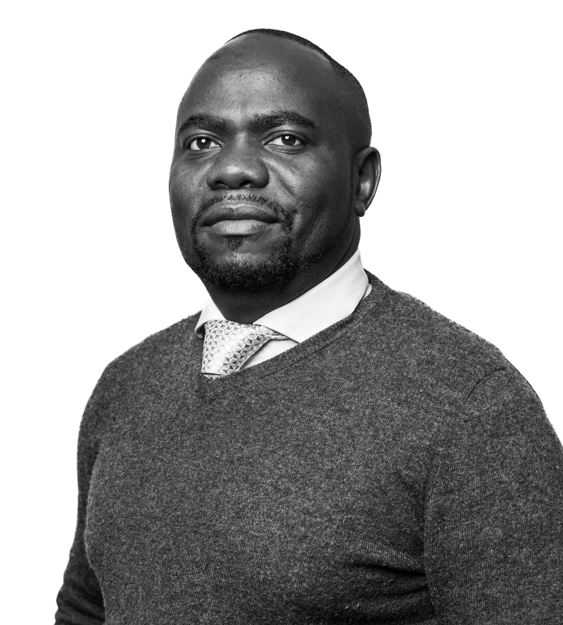 A black and white photo of a man wearing a sweater and tie.