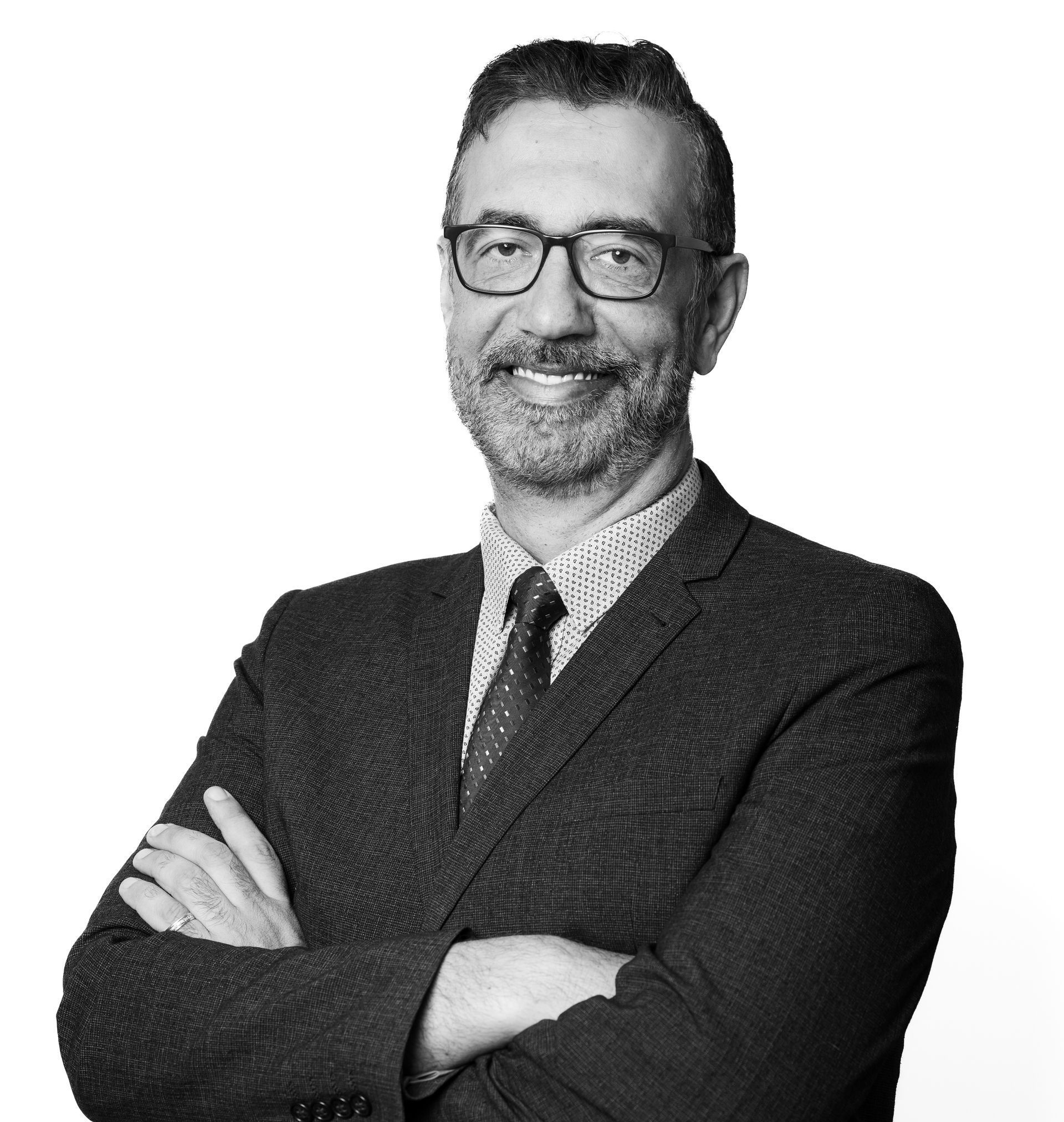 A man in a suit and tie with his arms crossed is smiling in a black and white photo.