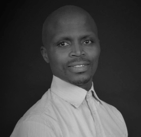 A man in a white shirt is smiling in a black and white photo.