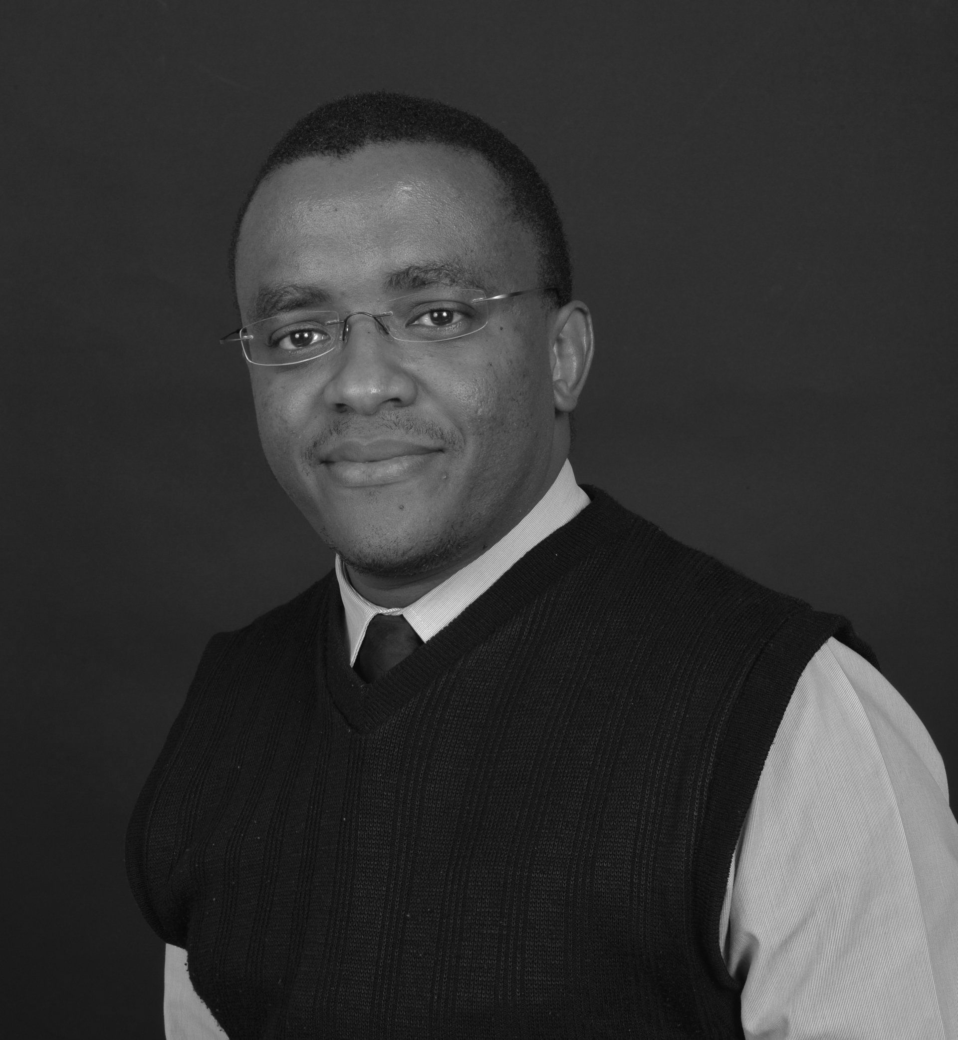 A black and white photo of a man wearing glasses and a vest.
