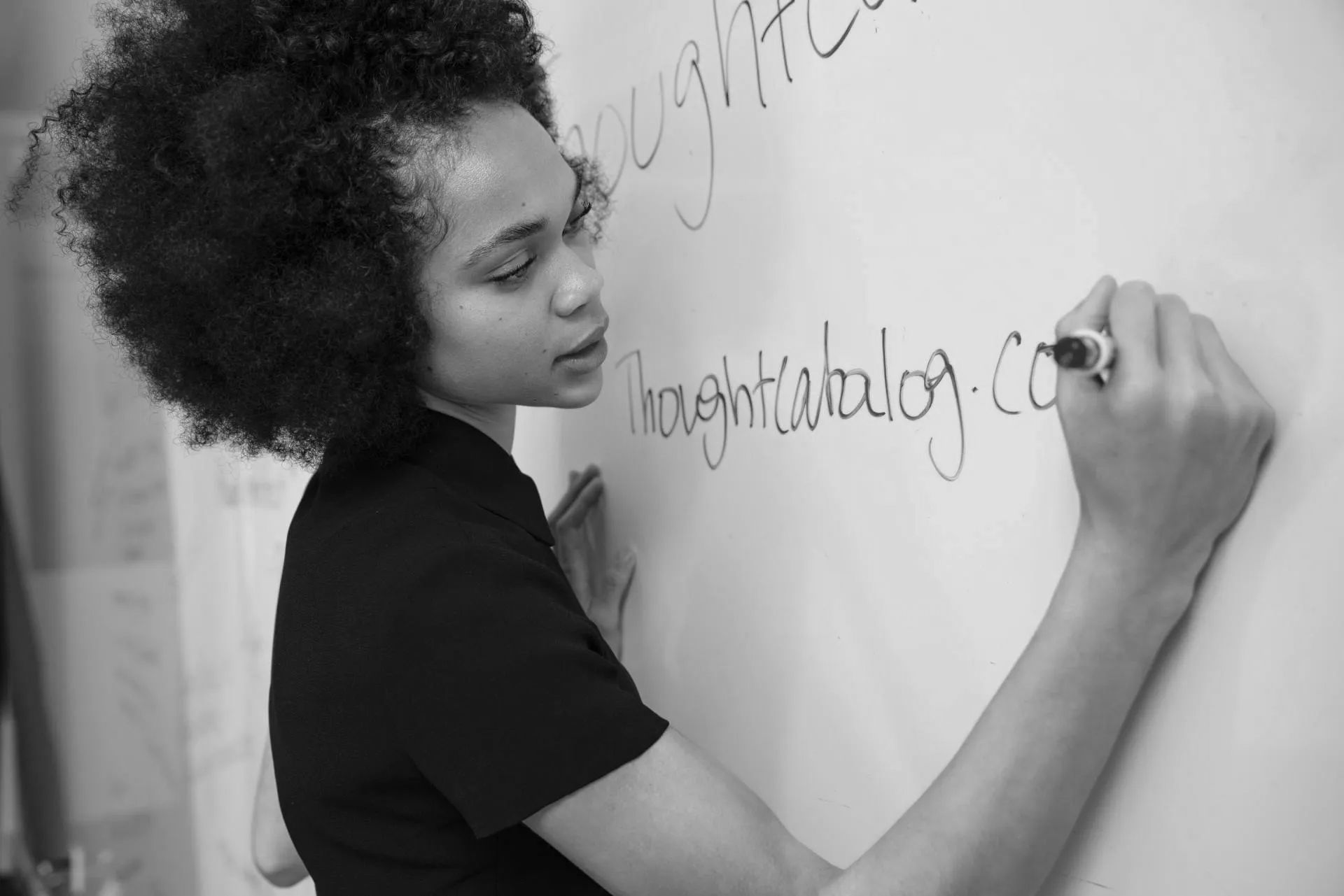 A black and white photo of a woman writing on a white board